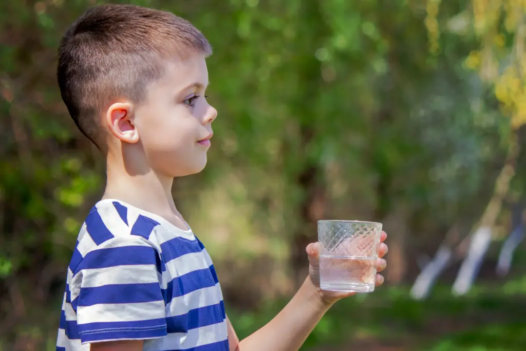 A young boy with a white and blue striped shirt holds a half-full glass of water.